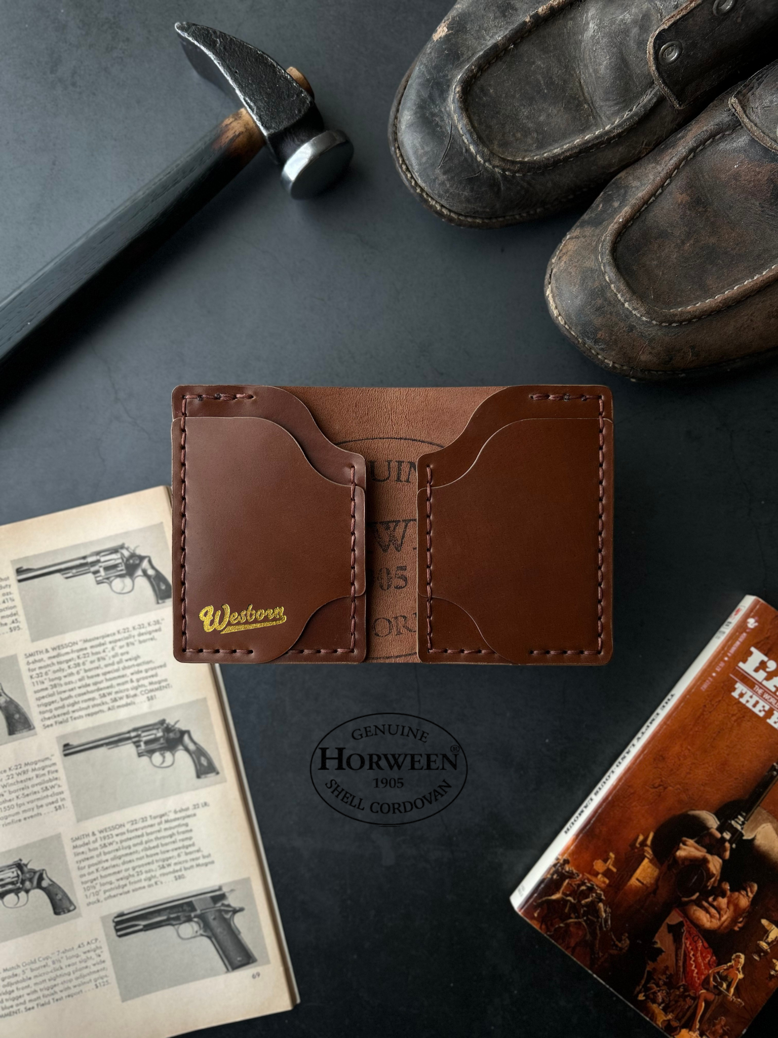 Brown leather wallet on a dark surface with a hammer, book, and cowboy boot.