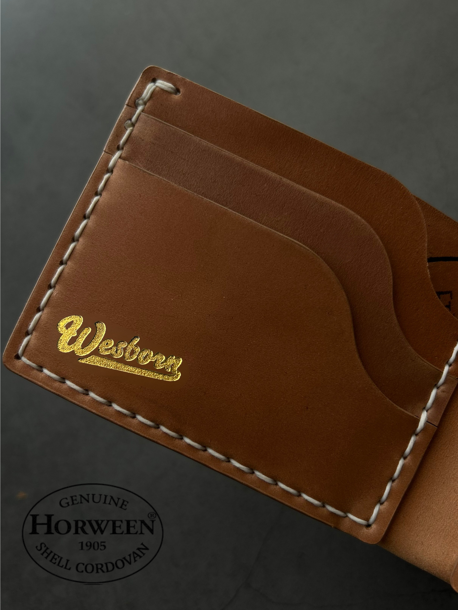 Brown leather wallet with gold stitching on a dark background