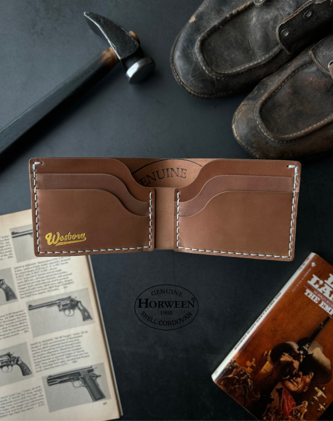 Brown leather wallet on a dark surface with a book and other items.